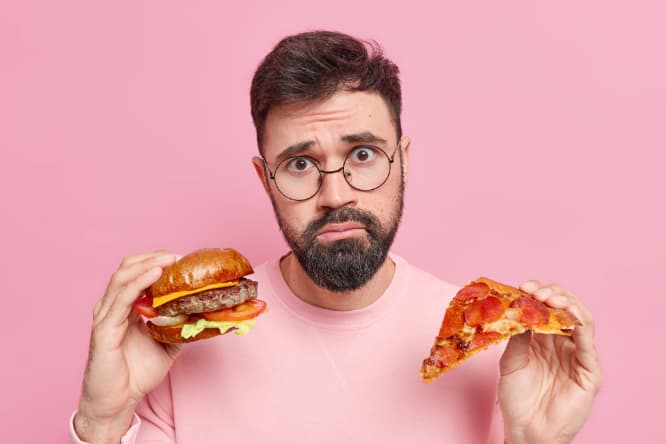 Anemia-cauzele-cele-mai-frecvete-barbat-cu-barba-ochelari-tricou-roz-hamburger-felie-de-pizza-fundal-roz Anemia-cauzele-cele-mai-frecvete-barbat-cu-barba-ochelari-tricou-roz-hamburger-felie-de-pizza-fundal-roz